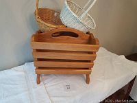 Photo showing solid oak magazine rack with two wicker baskets placed on top on a white cloth background.