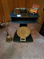 Front view of black TV stand with fireplace tool set to the left and decorative items on top and base.