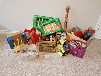 Overall view of various Christmas items including candles, bows, ornaments, a wooden crate, and boxes of outdoor flood lights packed together on carpeted floor.