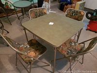 Square folding card table in good condition with four matching folding chairs, chairs have padded floral camouflage upholstery.