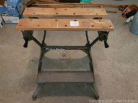 Front view of portable workbench with wooden top, green metal legs, and clamps visible