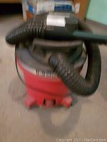 Front view of red and black 6.5 gallon wet/dry shop vacuum with hose wrapped on top and wheels at the base.