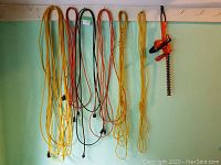 Photo showing four electrical cords and orange electric hedge trimmer hanging on wall