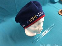 Navy blue and red Roots 2002 Olympic adjustable cap shown from front angle, displaying embroidered USA 2002 Olympic text and logos.