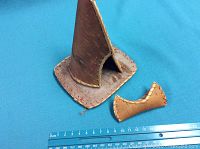 Two handcrafted miniature birch bark items, a small canoe and a small teepee model, placed on a blue background with a ruler for scale.