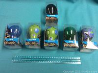 Six packaged light bulbs displayed against a blue background with a ruler for scale. Three contain solid color light bulbs (blue, black, green) and three contain hand painted light bulbs with colorful circular patterns.