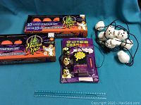 Two boxed sets of 10 Halloween light pumpkin string lights with Halloween Haunts branding, packaged voice changer device in original packaging with skull design, and a string of skull-shaped lights laid out against a blue background with measuring ruler for scale.