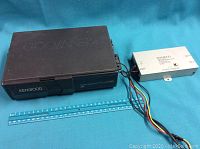 Black Kenwood CD car stereo unit with wiring next to a ruler for size reference