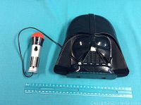 Darth Vader Voice Changer helmet with connected wired microphone placed on blue surface next to a ruler for size reference.