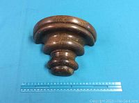 Front view of wooden wall sconce on blue background with ruler showing size.