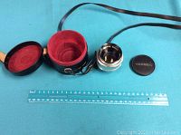 Lens, lens cap, and case laid out next to a ruler showing length scale