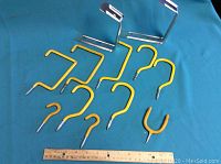 Photo of 10 yellow metal hangers and hooks of various shapes and sizes arranged on blue cloth with a ruler for scale.