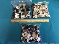 Three large resealable plastic bags filled with assorted buttons placed above a ruler for scale.