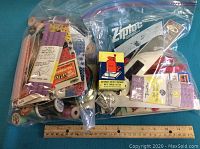 Photo displaying two large resealable plastic bags filled with various sewing supplies including thread spools, zippers, braiding trims, all laid on a teal surface with a wooden ruler for scale.
