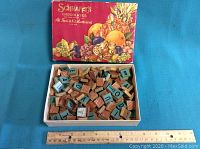 Wooden letter blocks in open Schraffts Chocolates box with ruler for size reference.