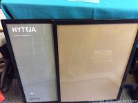 Two black IKEA NYTTJA picture frames shown side by side, one with insert, one empty.
