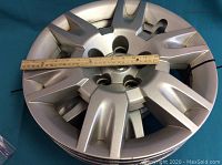 Photo showing one silver 17-inch Nissan hubcap with a ruler indicating size on top of it.