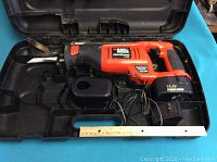 Black & Decker Fire Storm 14.4V cordless reciprocating saw, battery installed, and included battery charger inside open carrying case, ruler for scale.