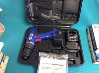 Blue and black Campbell Hausfeld cordless power drill with charger, battery, and instruction manual in black carrying case.