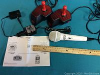 Two joystick controllers, American Idol microphone, and Game Boy charger with manual laid out on a blue surface.