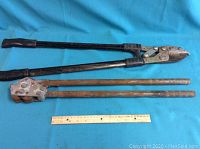 Two large metal hand tools, a clipper and crimper, placed side by side with a ruler showing their length (~24 inches).