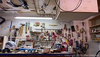 Wide view of workbench with various hand tools hung on pegboard, tools on the bench including hammers, clamps, and a red desk lamp.