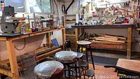 View of two wooden workbenches in a tool room with stools, scrap wood underneath, and items on bench tops