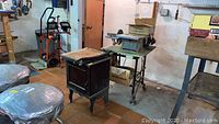 Photo of the disc sander on a green metal stand with the black guillotine cutter cabinet nearby in a workshop setting.