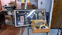 Framed military patches and medals shown with a box of loose patches and decals in a workshop setting.