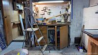 Wide view of workbench area with ladder and storage cabinet below bench in workshop environment.