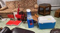Wide view of lot showing cooler, two red bleacher chairs, blue humidifier, wicker picnic basket, wooden trays, and various other items.