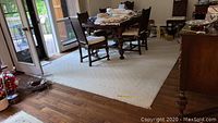 Full view of the light-colored area rug with geometric textured pattern placed on hardwood floor beneath dining table and chairs.