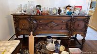 Front view of vintage solid oak buffet with various decorative items on top, showing carved panel doors and drawer handles.
