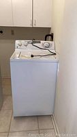 Front view of white GE top load washing machine, showing full appliance from floor to top control panel.