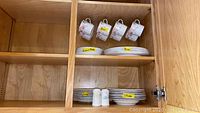 Kitchen cabinet with 4 hanging floral design cups and stacked plates with labels