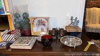 Overview of lot items displayed on table including tea cup and saucer, inlaid box, coasters, trivets, and decorative items