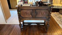 Front view of the vintage oak hutch showing the carved legs and unique cabinet doors with knob handles on a wooden floor.
