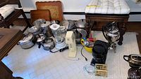 Wide view showing Waring Pro Blender with glass jar, multiple stainless steel pots and pans, and coffee makers grouped on floor.