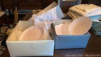 Two boxes each containing neatly wrapped white embossed dishes with butterfly and floral patterns, partially visible with bubble wrap and tissue paper for protection.