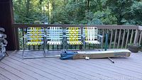 Four vintage aluminum outdoor chairs arranged on deck with nature in background and a packaged outdoor umbrella lying in front