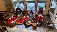 Overview of assorted Christmas decorations including prelit tree, Santa figures, wreaths, candles, poinsettias, ribbons, and ornaments displayed on wooden floor.