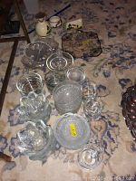 Top-down photo showing all items spread on carpet including glass bowls, plates, canisters, ceramic figurines, and crosses.