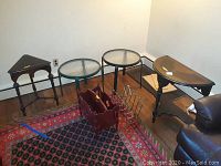 Wide shot showing two wood corner tables, two round glass tables, and two magazine racks on a rug in a corner room.