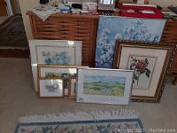 Overview photo of all seven framed artworks grouped leaning against furniture showing variety in size and style