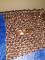 Tie clip placed on brown textured fabric with blue tape edges, showing overall item details.