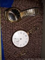 Photo showing Seiko wristwatch with dark dial and expandable gold-tone band alongside Waltham pocket watch and chain.