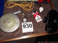 Showcases all lot items on brown carpet including vintage Excelsior Savings coin bank with key, Marlboro lighter, pipe lighter, metal fotoreel, thimble, white tape measure keychain, and silver metal capsule.