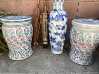 Photo showing two ceramic stools with floral designs, a repaired blue and white porcelain vase, and several decorative umbrellas and cane.