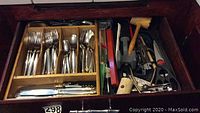 Drawer containing Oneida cutlery sets with gold-accented handles including forks, spoons, and knives, along with wooden and metal kitchen utensils on the right side.