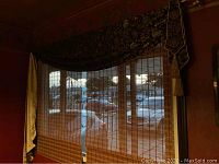 Photo showing bamboo roll-up blinds on a window with dark floral low valance inside room with reddish walls.